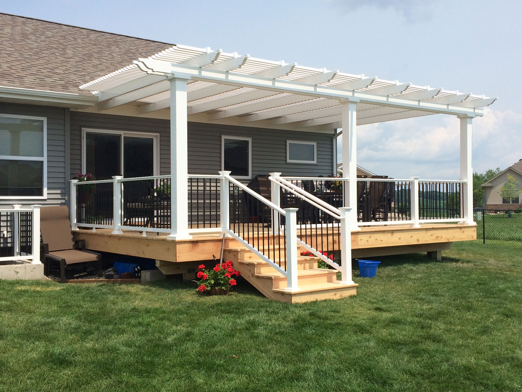 Attached pergola with white siding. There are steps that lead up from the yard to the covered deck area.